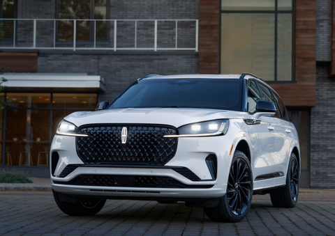 A white 2025 Lincoln Aviator® SUV is shown parked outside a modern building with gray brick and wood accents. | Johnson Brothers Lincoln in Temple TX