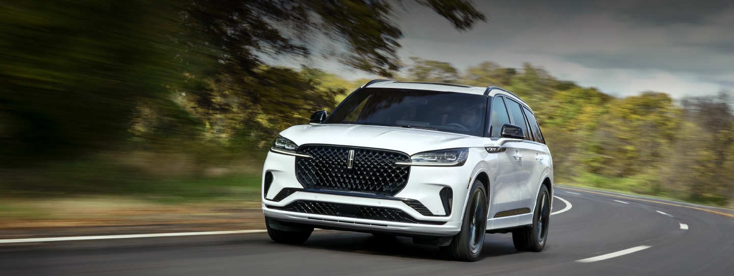 A white 2025 Lincoln Aviator® SUV is being driven down a road lined with trees. | Johnson Brothers Lincoln in Temple TX