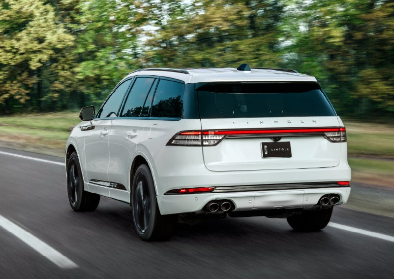 A white 2026 Lincoln Aviator® SUV is being driven away down a road lined with colorful trees. | Johnson Brothers Lincoln in Temple TX