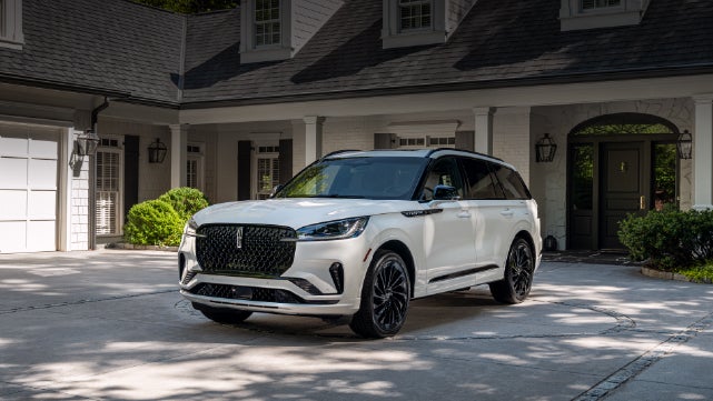 A white 2026 Lincoln Aviator® SUV is parked in the driveway of a luxury home. | Johnson Brothers Lincoln in Temple TX