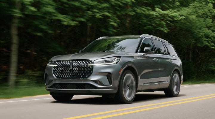 A 2027 Lincoln Aviator® SUV is being driven down a road lined with trees. | Johnson Brothers Lincoln in Temple TX